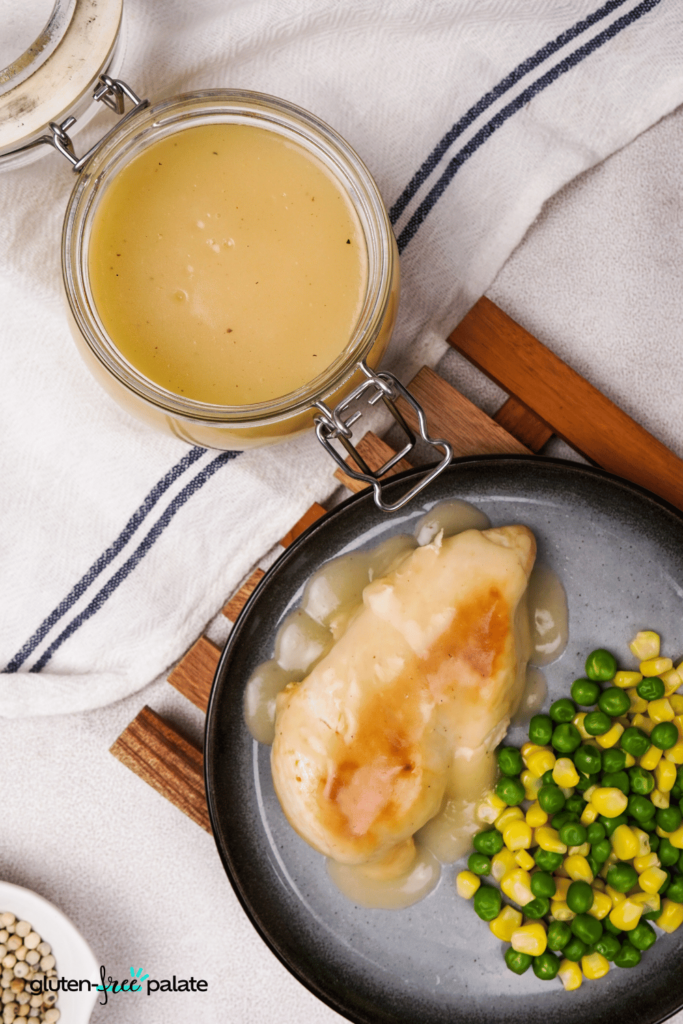 A glass jar of gluten-free gravy. A slice of turkey, covered in rich gravy, on a plate with peas and corn.