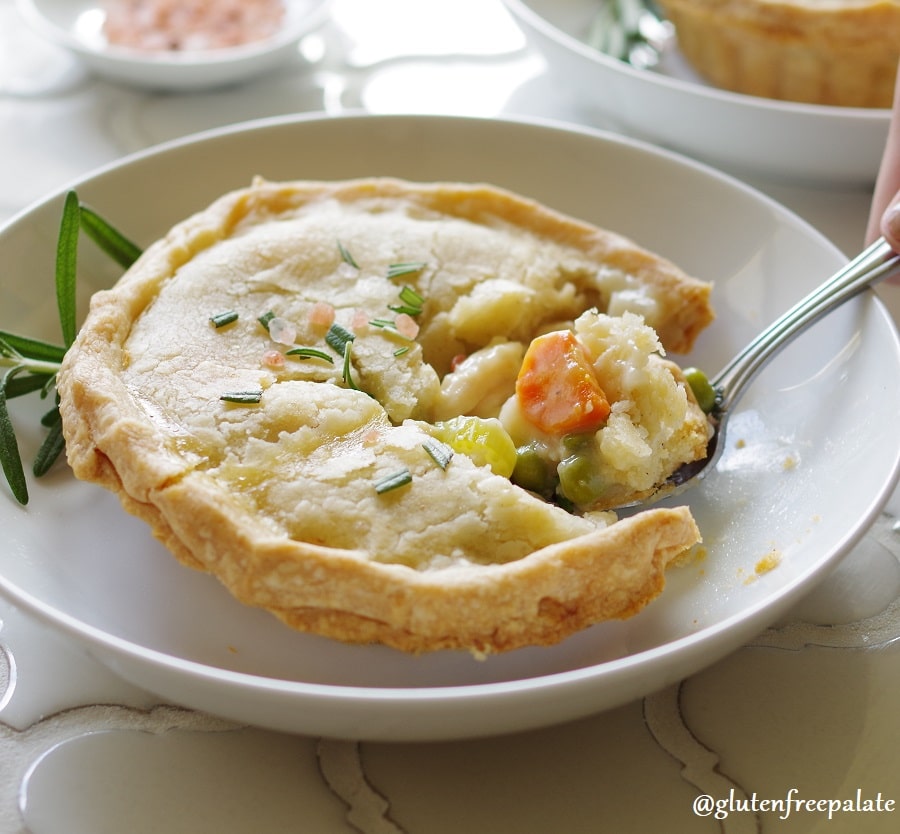 a close up of a Gluten-Free Chicken Pot Pie topped with salt and rosemary on a white plate, with a spoon taking a bite out
