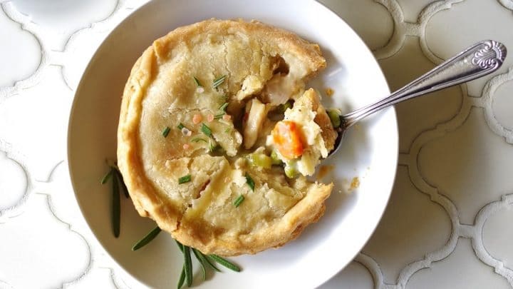 a close up of a Gluten-Free Chicken Pot Pie topped with salt and rosemary on a white plate, with a spoon taking a bite out