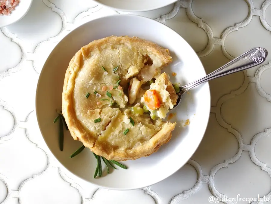 a top down view of a Gluten-Free Chicken Pot Pie topped with salt and rosemary on a white plate, with a spoon taking a bite out