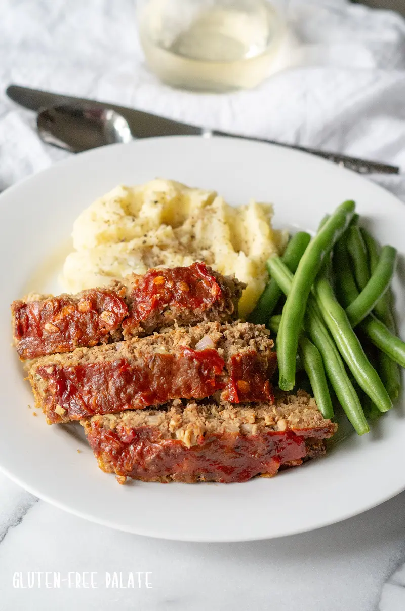 side view of sliced Gluten-Free Meatloaf on a white plate with mashed potatoes and green beans