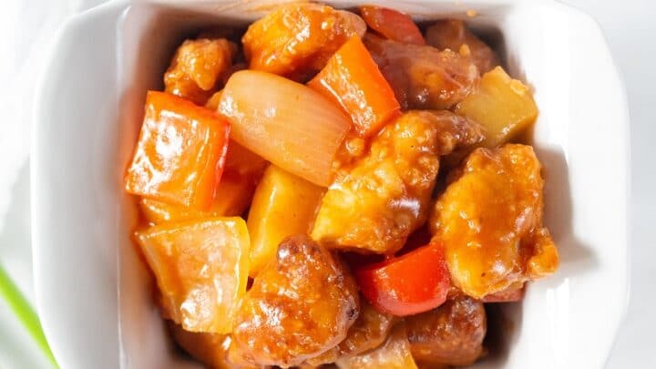 Gluten Free Sweet and Sour Chicken in a white dish with a spring of onion next to it