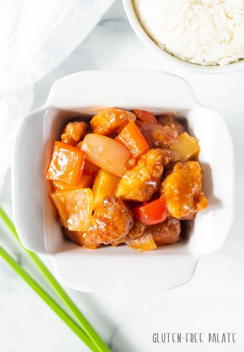 Gluten Free Sweet and Sour Chicken in a white dish with a spring of onion next to it