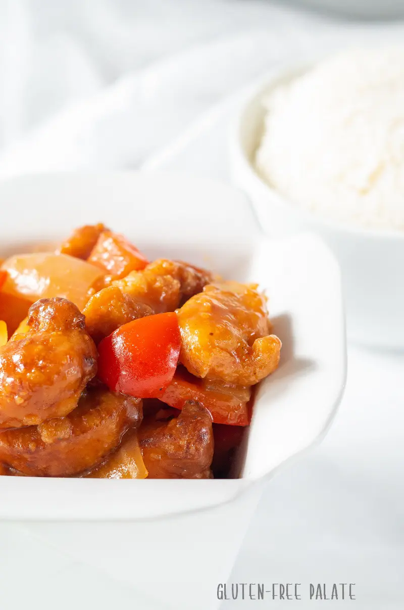 Gluten Free Sweet and Sour Chicken in a white dish with a bowl of rice in the background