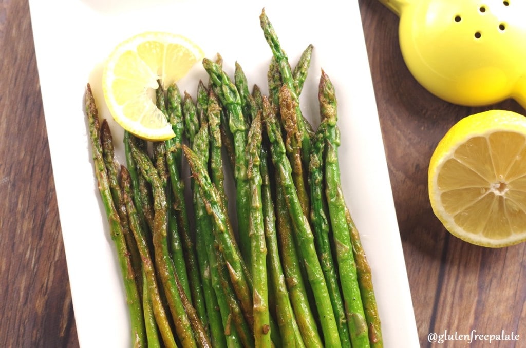 Asparagus spears on a white plate with a slice of lemon, with a wedge of lemon on the side
