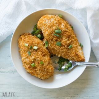a close up of two breaded chicken breasts topped with sliced green onion on a white plate
