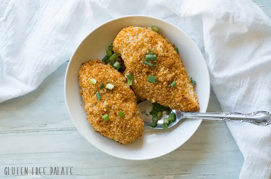 two breaded chicken breasts topped with sliced green onion on a white plate with a spoon