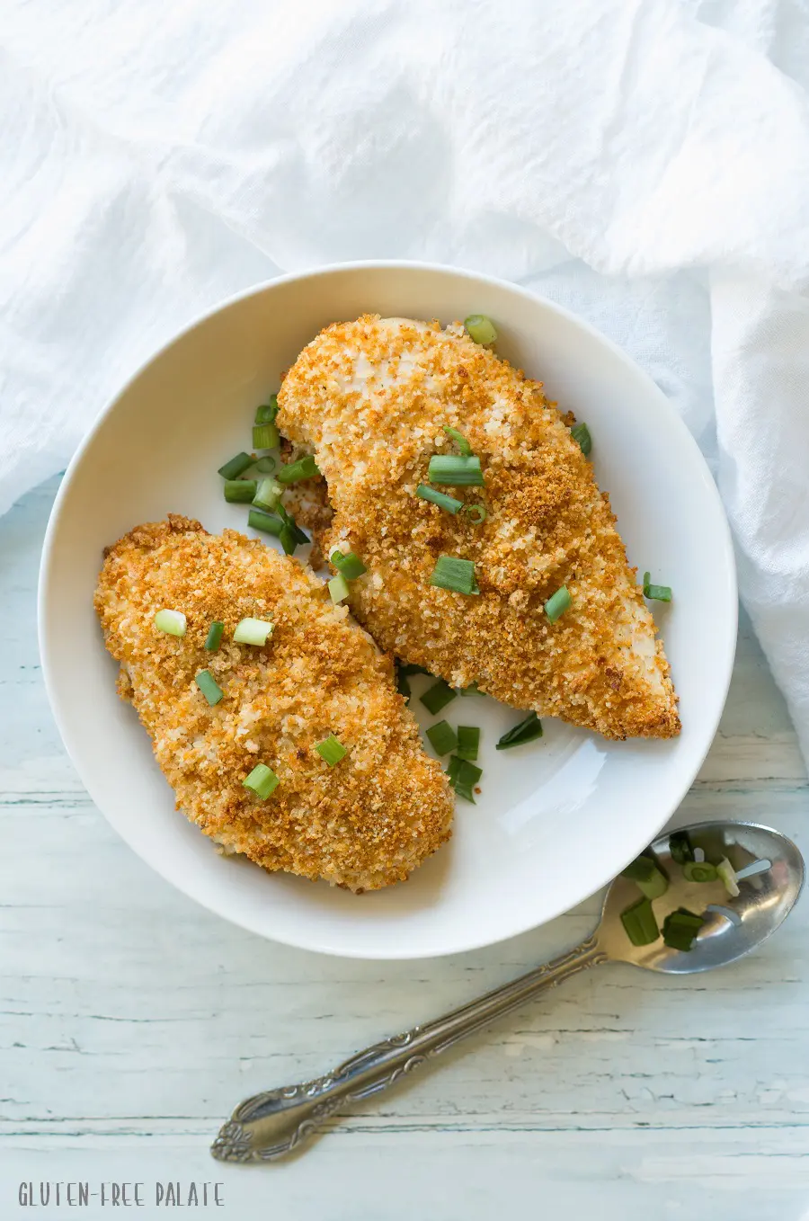 top view of two gluten-free breaded chicken breasts topped with sliced green onion on a white plate