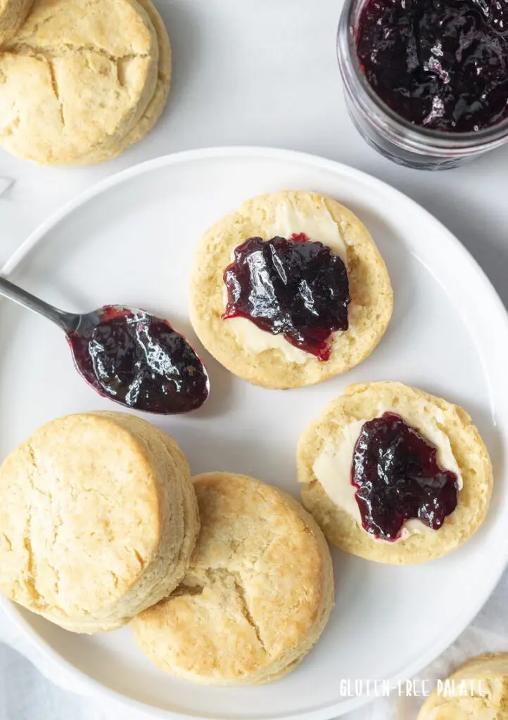 Three Gluten-Free Biscuits on a white plate with butter and grape jam