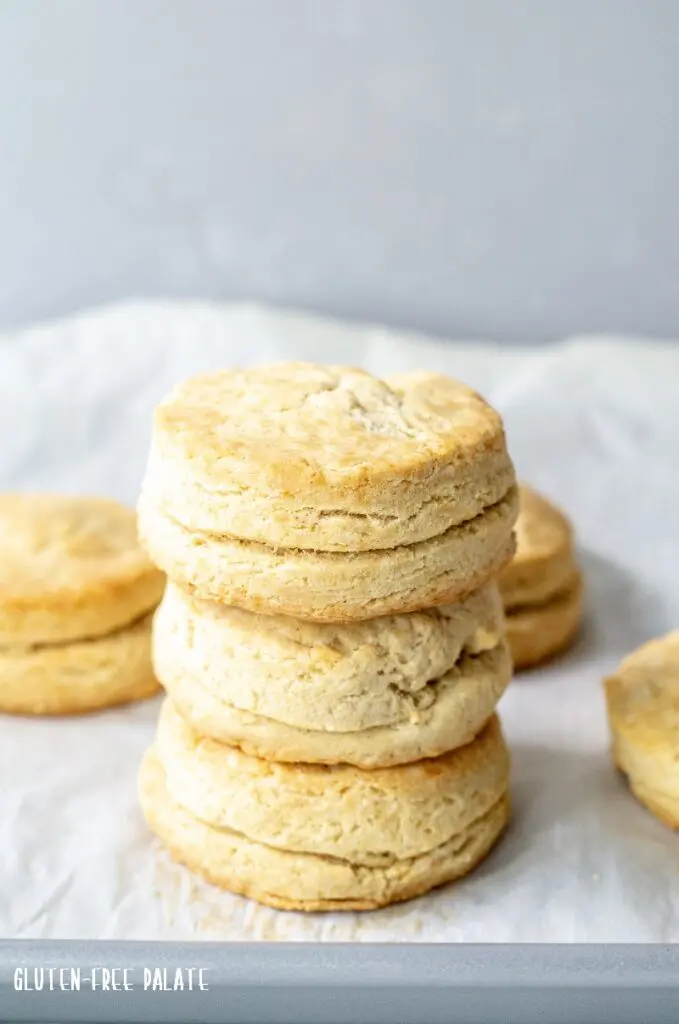 Three gluten-free biscuits stacked on white parchment paper with three biscuits in the background