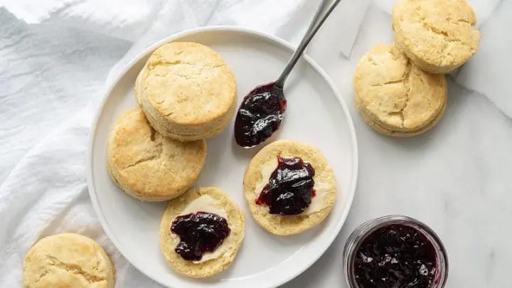 Three Gluten-Free Biscuits on a white plate with butter and grape jam