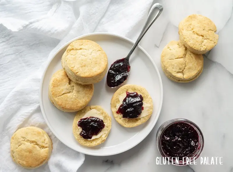 Three Gluten-Free biscuits on a white plate with butter and grape jam
