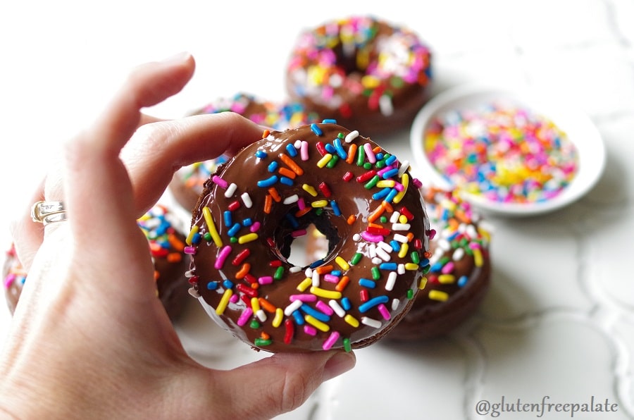 a hand holding a chocolate donut with colored sprinkles