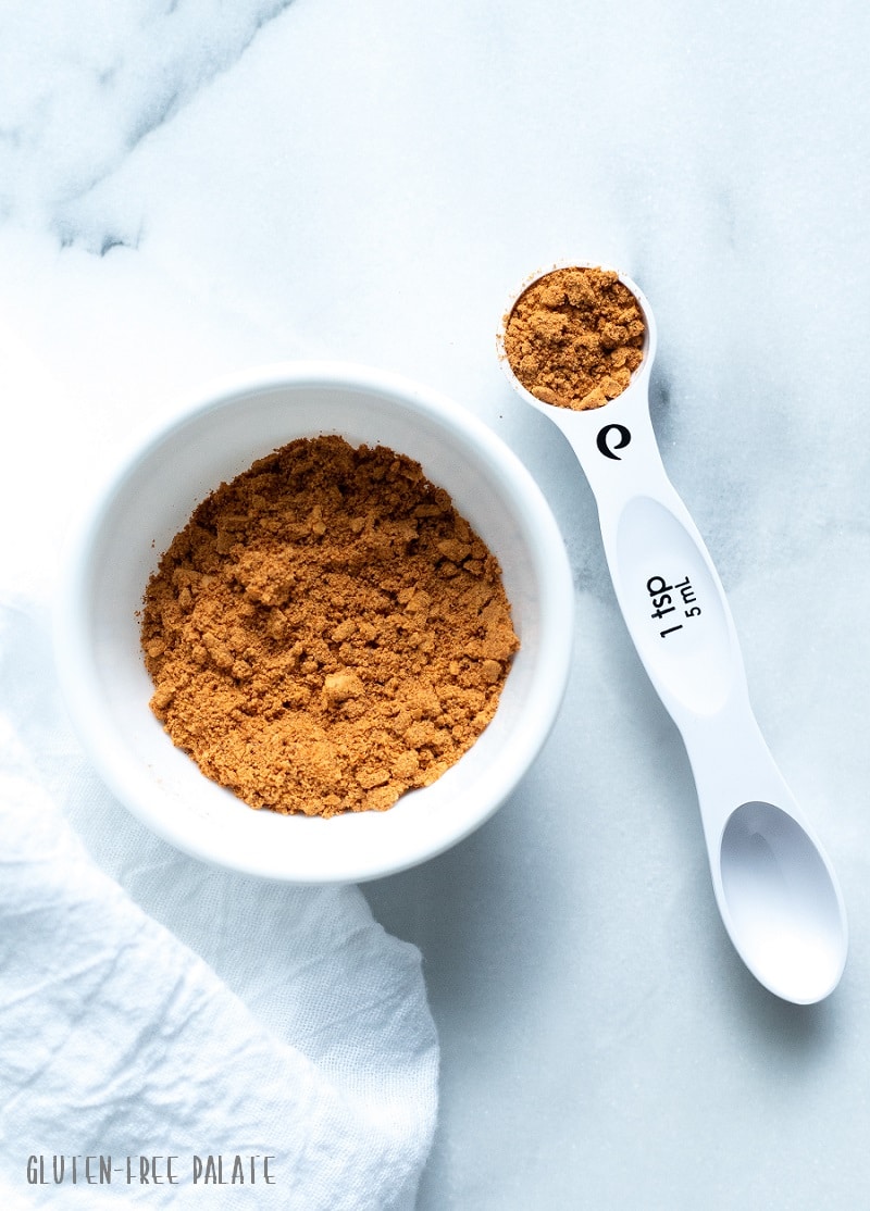 gluten free taco seasoning in a white bowl next to a measuring spoon with taco seasoning