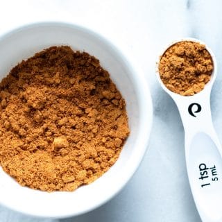a close up of gluten-free taco seasoning in a white bowl next to a measuring spoon with taco seasoning in it