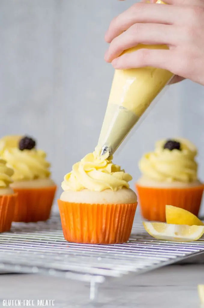 a hand piping yellow frosting onto a lemon cupcake
