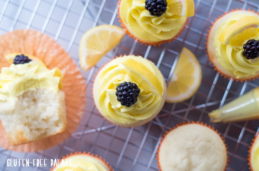 a top down view of lemon cupcakes topped with yellow frosting and a blackberries on a wire cooling rack