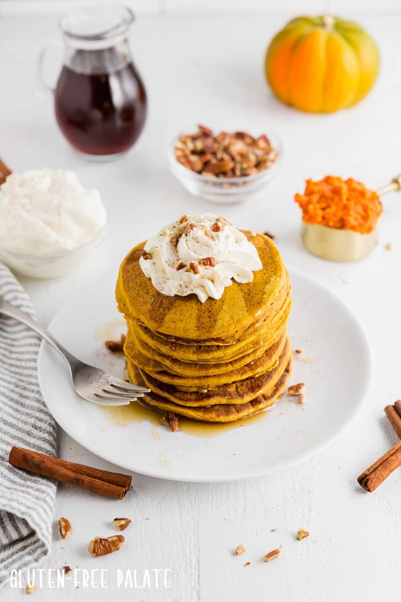 a stack of gluten free pumpkin pancakes topped with whipped cream