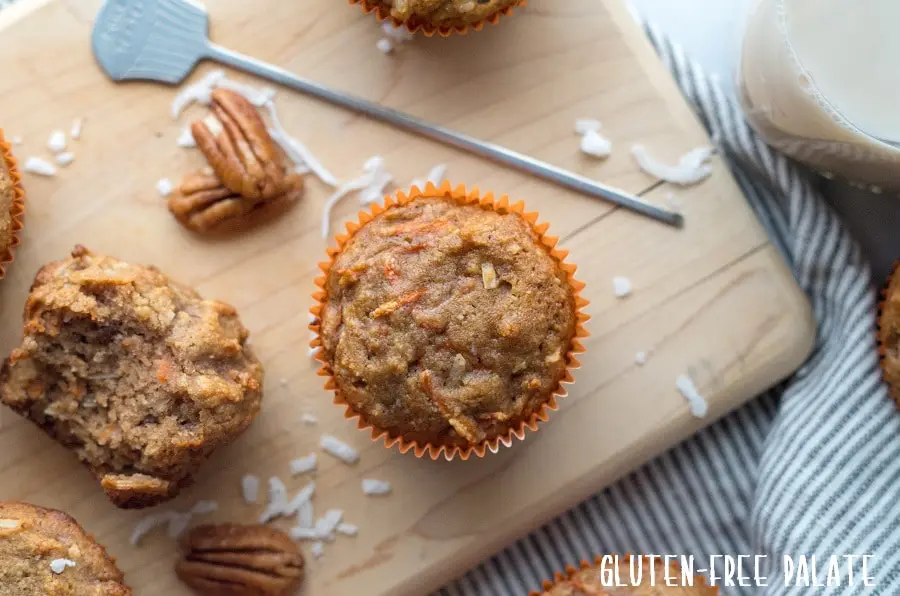 a top down view of a paleo carrot muffins on a cutting board next to a muffin with a bite out