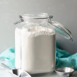 a close up of a jar of gluten free flour next to measuring cups and a blue kitchen towel