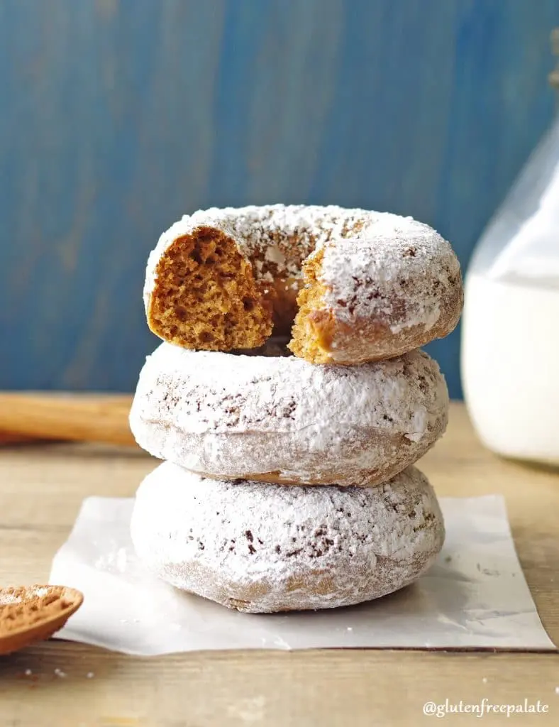 three gingerbread donuts coated in powdered sugar stacked, the top donut has a bite out