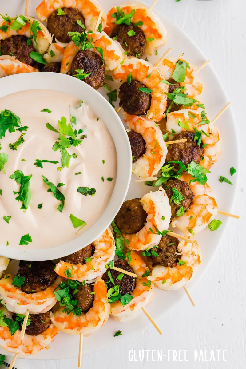 a close up of sausage and shrimp on toothpicks around a bowl of dipping sauce