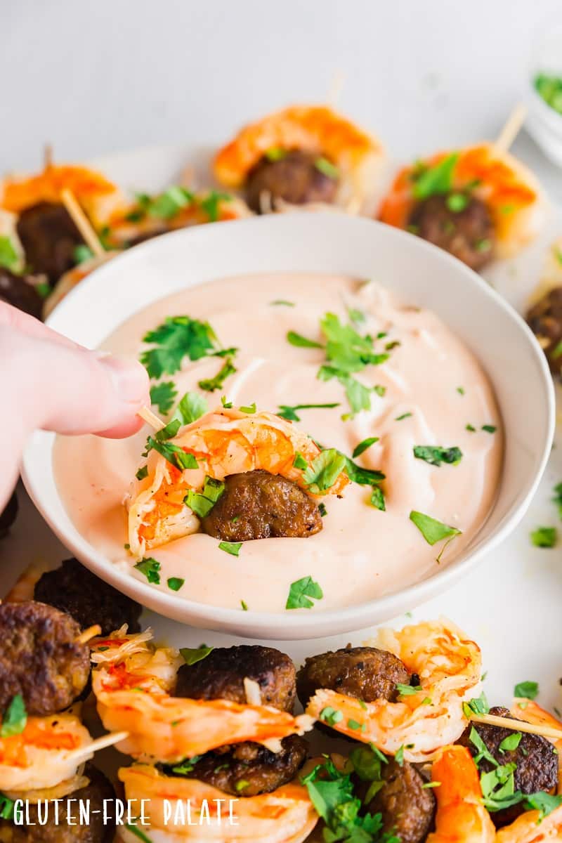 a hand dipping sausage and shrimp appetizer into dipping sauce