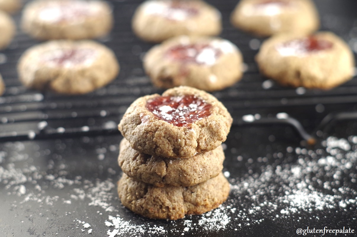 a close up of three paleo strawberry thumbprint cookies stacked in front of a wire cooling rack with cookies