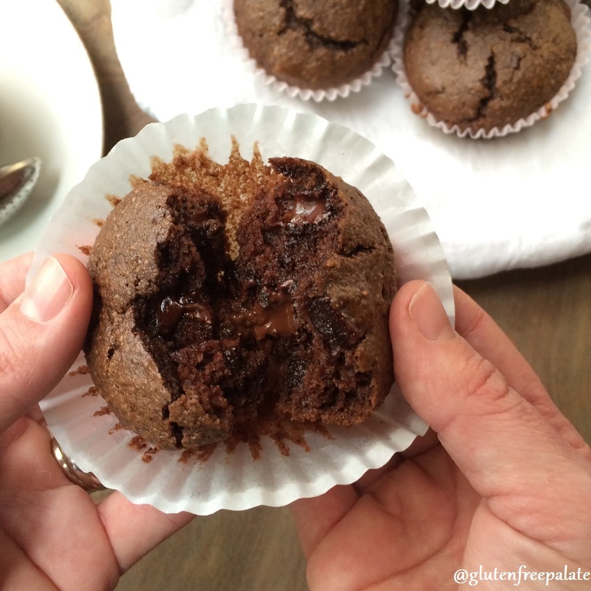 a hand holding a gluten free chocolate muffin, breaking it open to show the texture