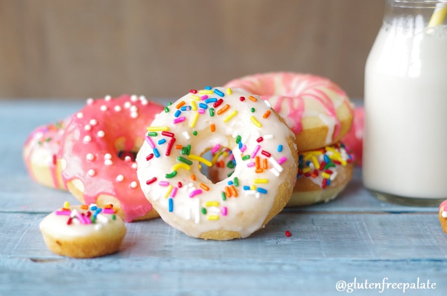 gluten free vanilla donuts with colored icing and colored sprinkles arranged next to a jar of milk