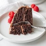 a close up of a slice of gluten free chocolate cake on a white plate with a fork and raspberries