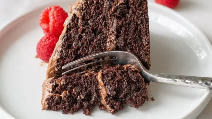 a close up of a slice of gluten free chocolate cake on a white plate with a fork and raspberries