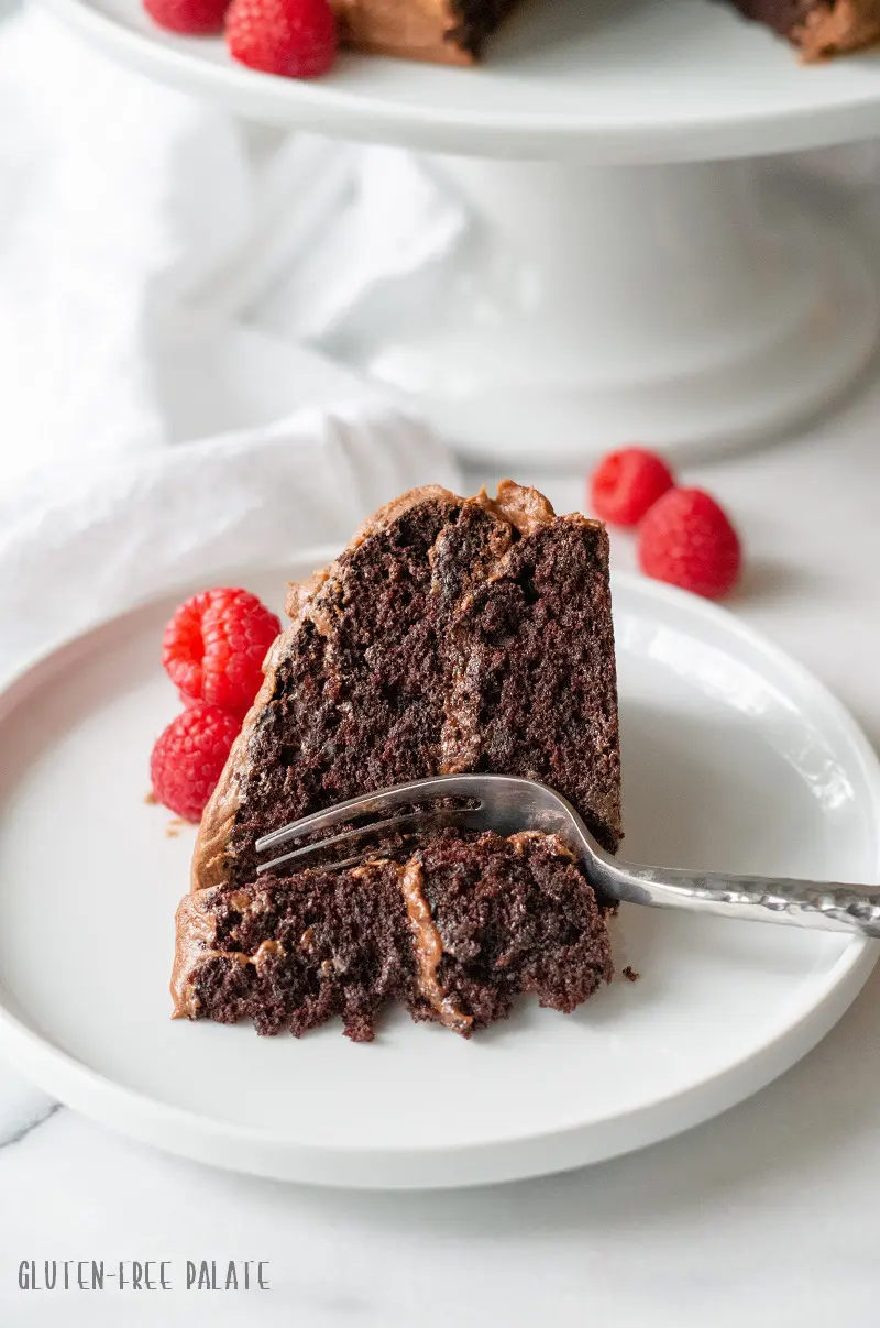 a slice of gluten free chocolate cake on a white plate with a fork and raspberries