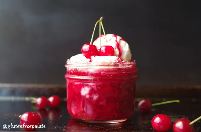 a close up of cherry filling in a jar topped with cobbler, vanilla ice cream, and cherries