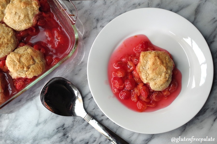 cherry cobbler on a white plate next to a serving spoon