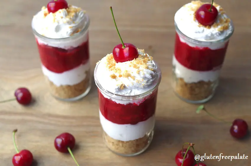 a side view of three shot glasses filled with layers of graham cracker crumbs, whipped cream, cherry pie filling