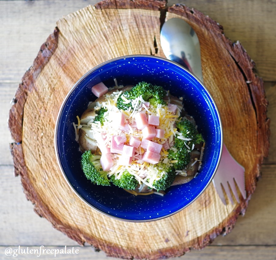 a baked potato covered with broccoli, cheese, and diced ham in a blue bowl