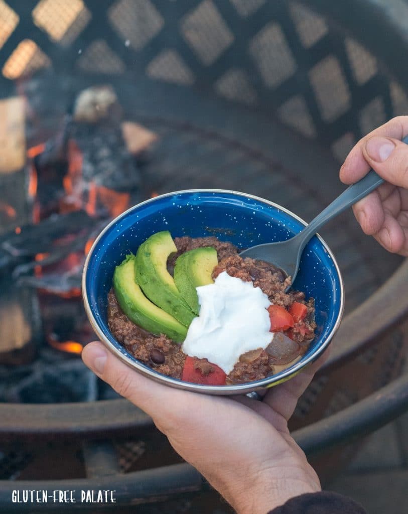 a spoon dipping into chilli next to a camp fire