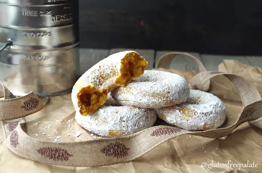 Three pumpkin donuts with powdered sugar stacked with half of a donut on top