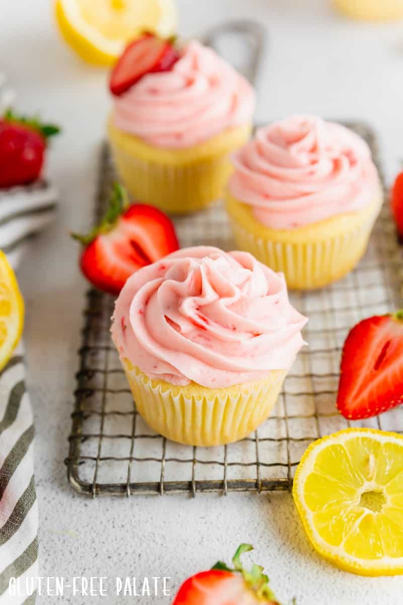 A gluten-free strawberry cupcakes with strawberry frosting on a cooling rack with other gluten-free strawberry cupcakes.