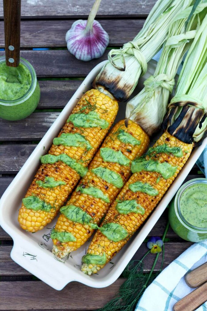 corn on the cobb with green sauce in a white dish