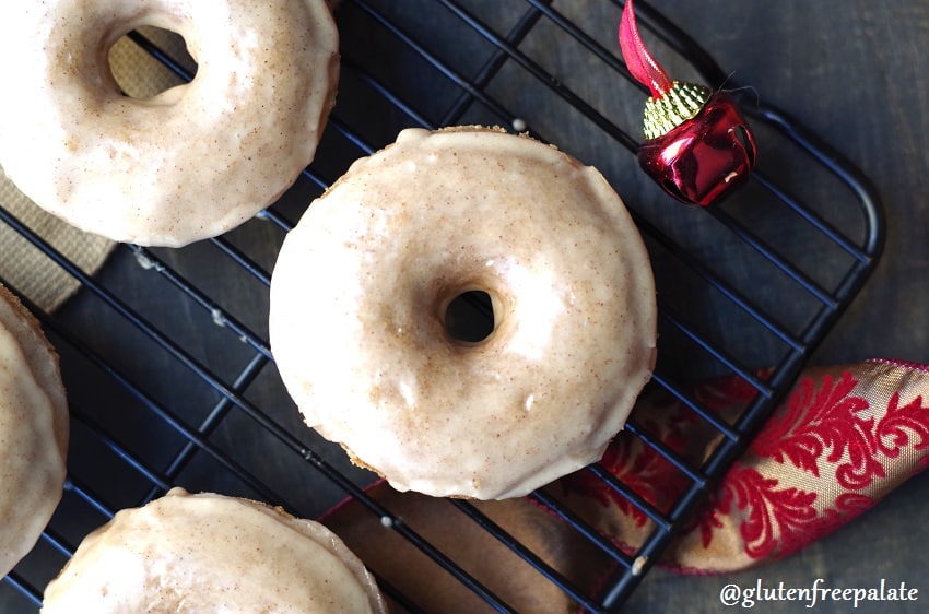 gluten free chai donuts on a wire rack next to a red bell and a holiday ribbon