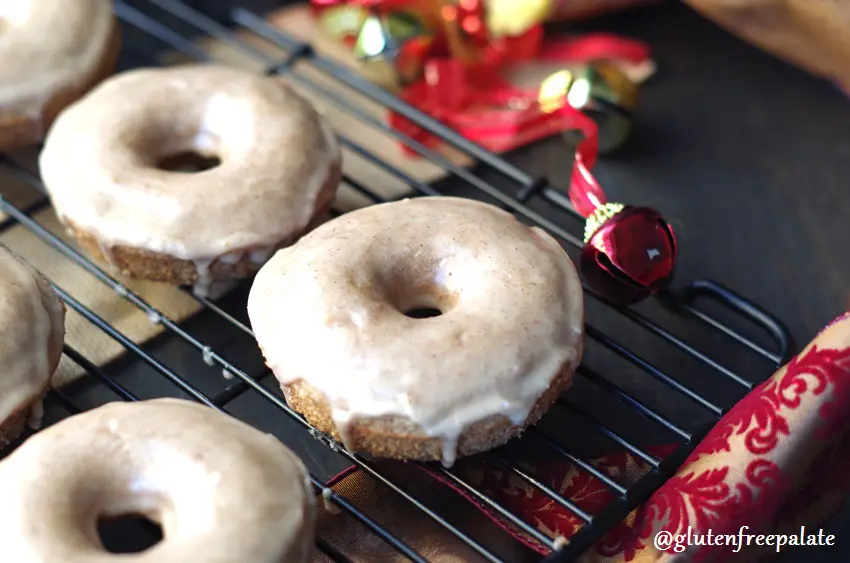 a side view of gluten free chai donuts on a wire rack next to a red bell and a holiday ribbon