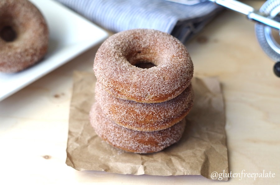a side view of gluten-free cinnamon sugar donuts stacked on a piece of brown paper