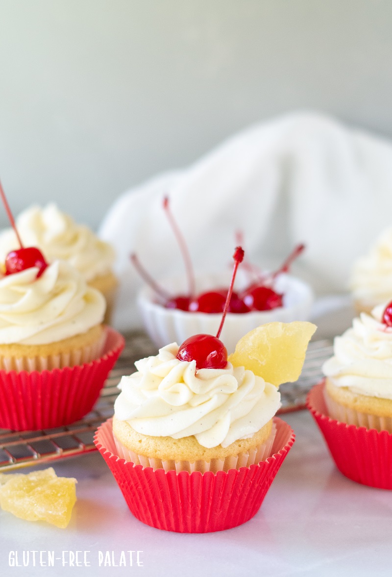 Gluten Free Pina Colada Cupcakes with a cherry on top in red paper liners