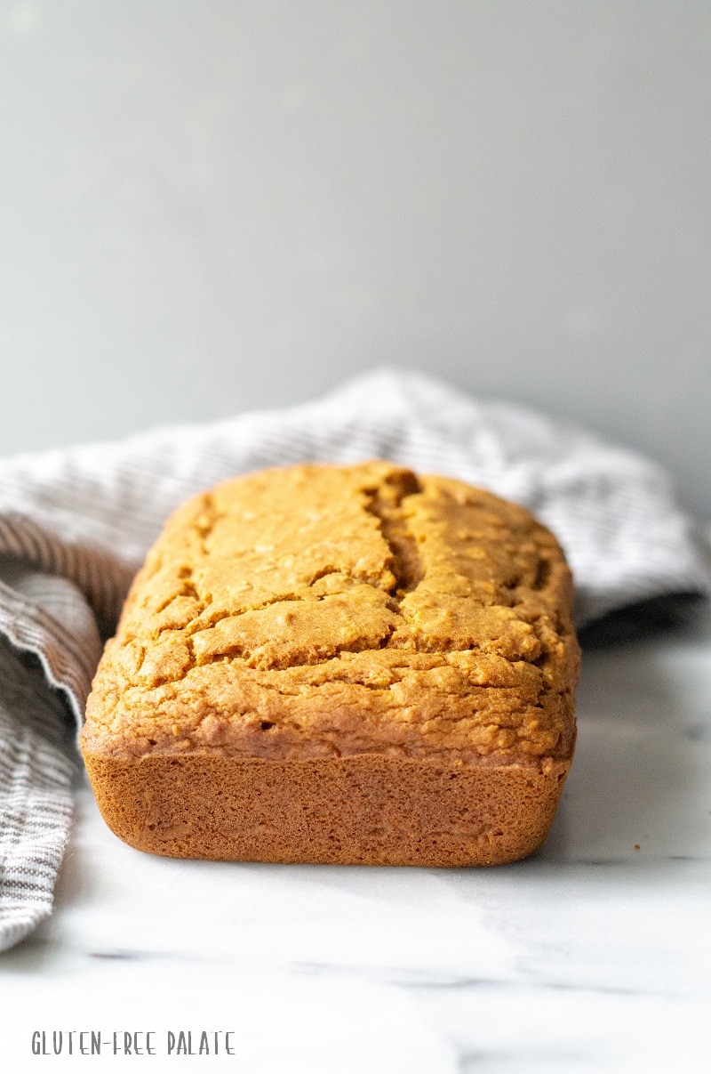 A loaf of gluten-free pumpkin bread on a white counter next to a strip towel