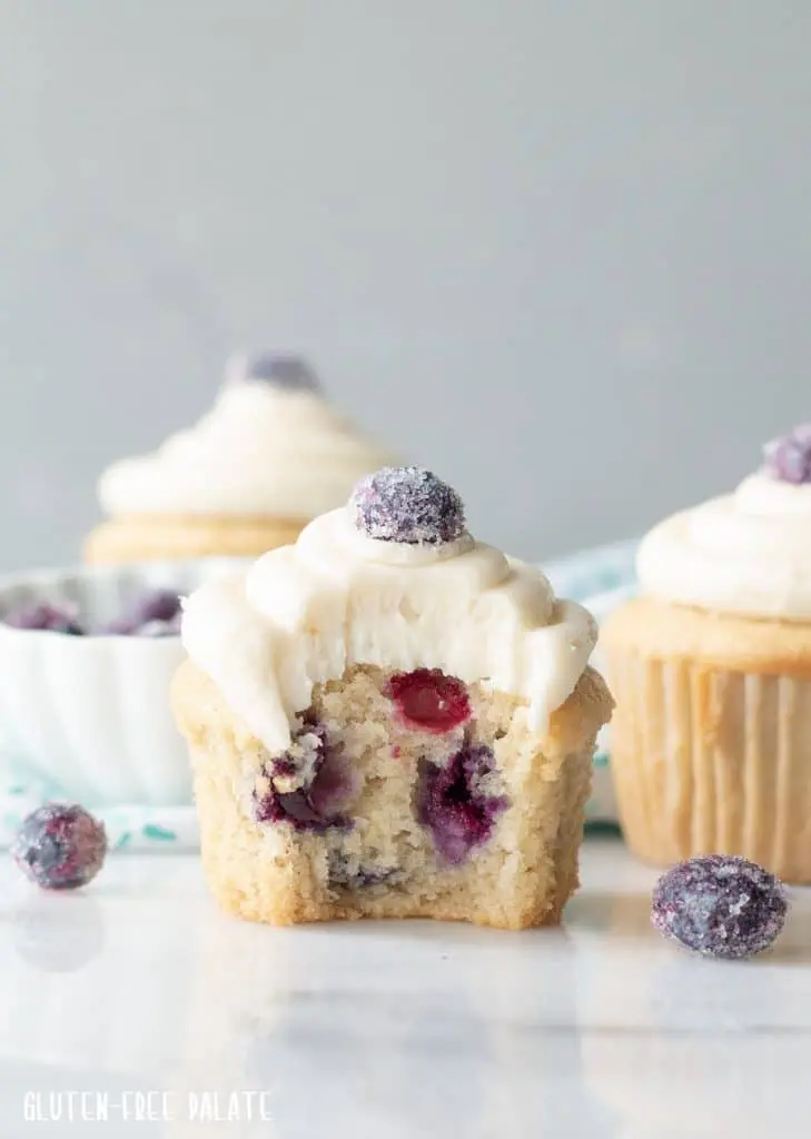 a close up of a blueberry cupcake with white frosting with a bite taken out