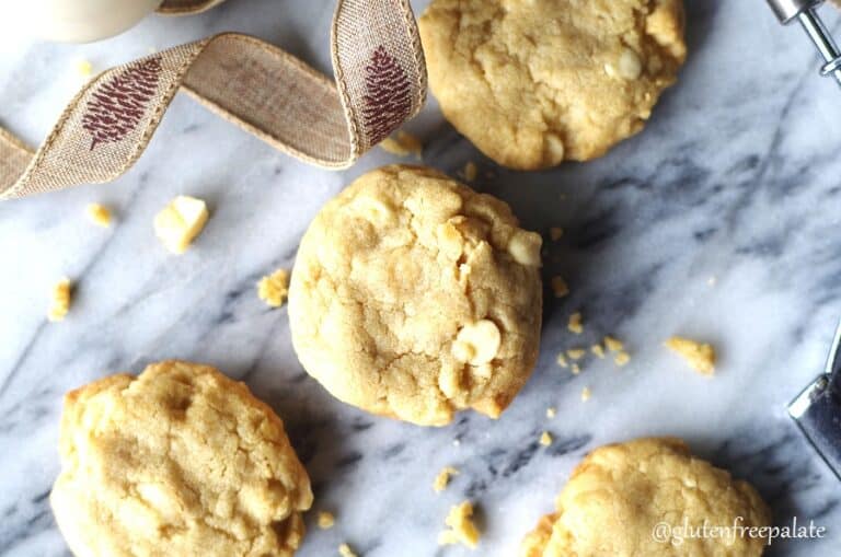 a close up of four gluten-free white chocolate macadamia cookies on a marble slab with a browni ribbon