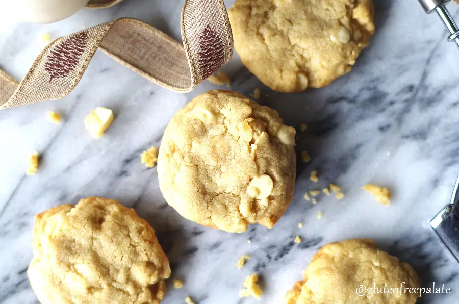 four gluten-free white chocolate macadamia cookies on a marble slab with a browni ribbon