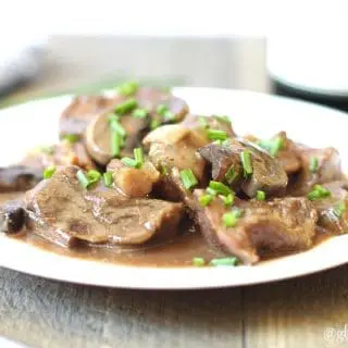 a close up of beef tips and sliced mushrooms in a sauce on a white plate